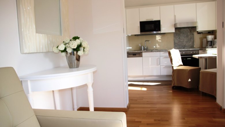 Altes Pförtnerhaus, © © Elisabeth Hofer Innenansicht eines modernen Wohnbereichs mit Küche und Blumen auf einem Tisch.