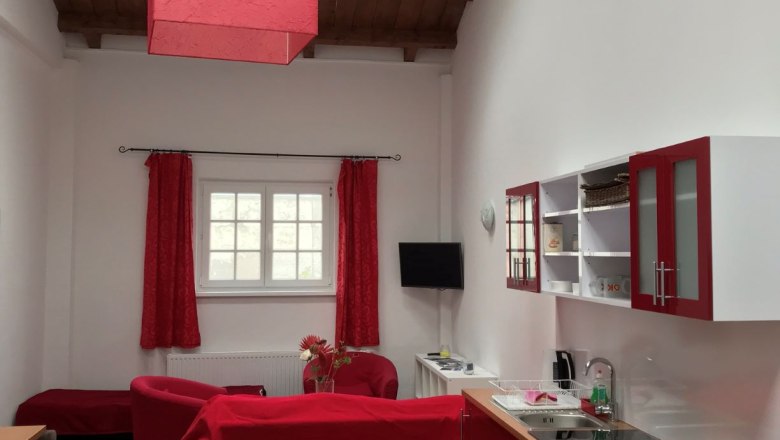 Wohn- und Essbereich in einem Loft mit roten M&ouml;beln und Holzbalkendecke.