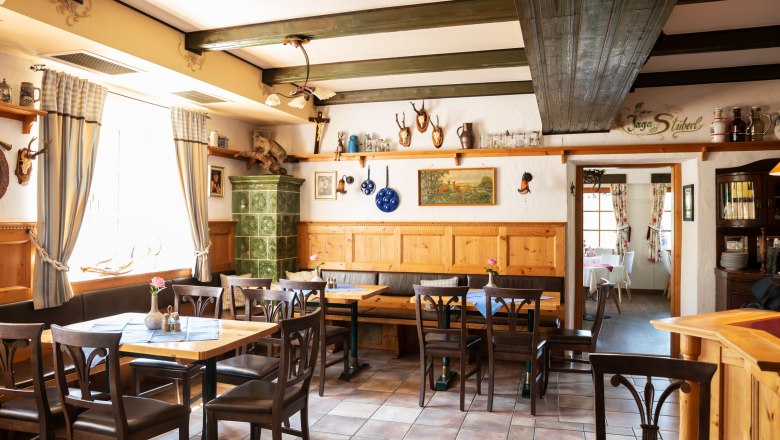 Gem&uuml;tliche Stube mit Holzm&ouml;beln, Kachelofen und Jagdtroph&auml;en an den W&auml;nden.