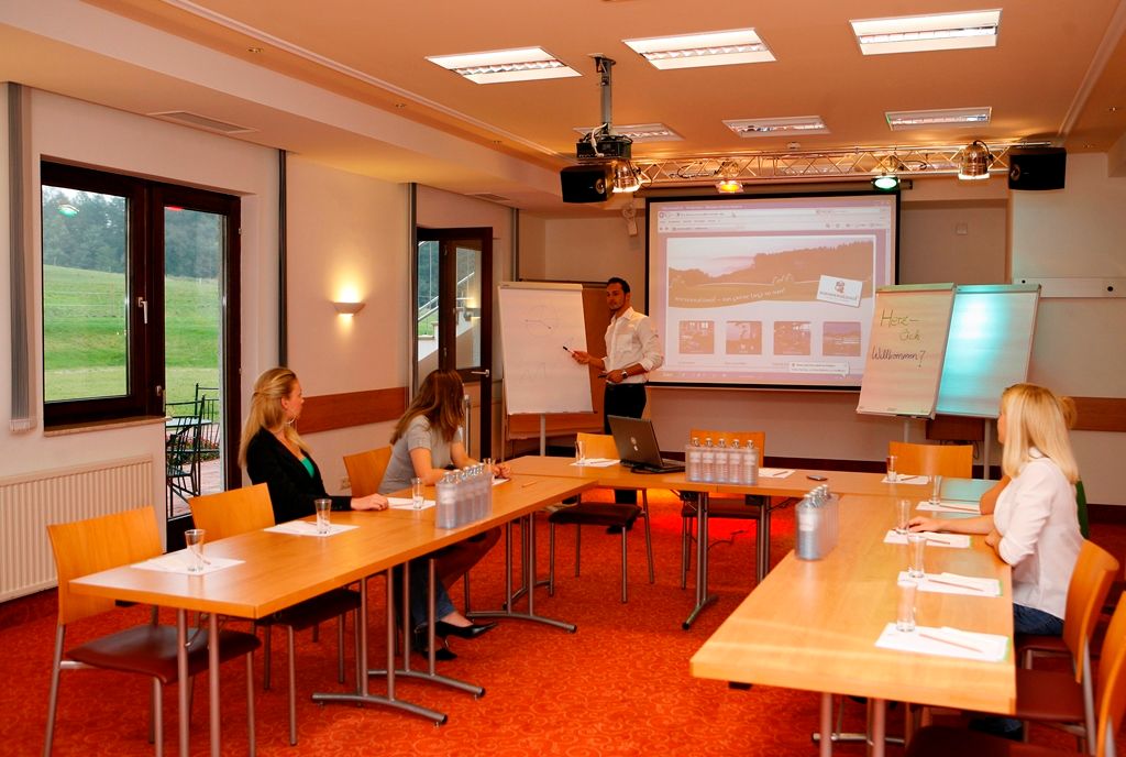 Seminarhotel Wienerwaldhof: Seminarraum mit Präsentation, Flipcharts und vier Teilnehmenden an Tischen.