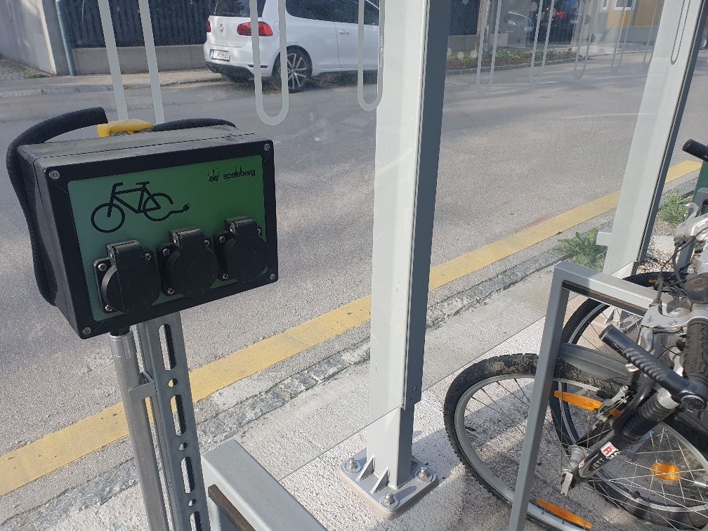 E-Bike Ladestation mit Steckdosen und Fahrrädern daneben.