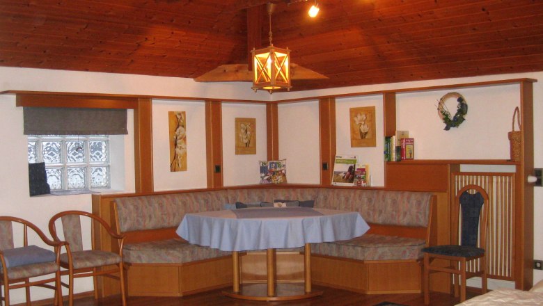 Gemütliche Sitzecke mit Holzmöbeln und blauer Tischdecke in einem Raum mit Holzdecke.