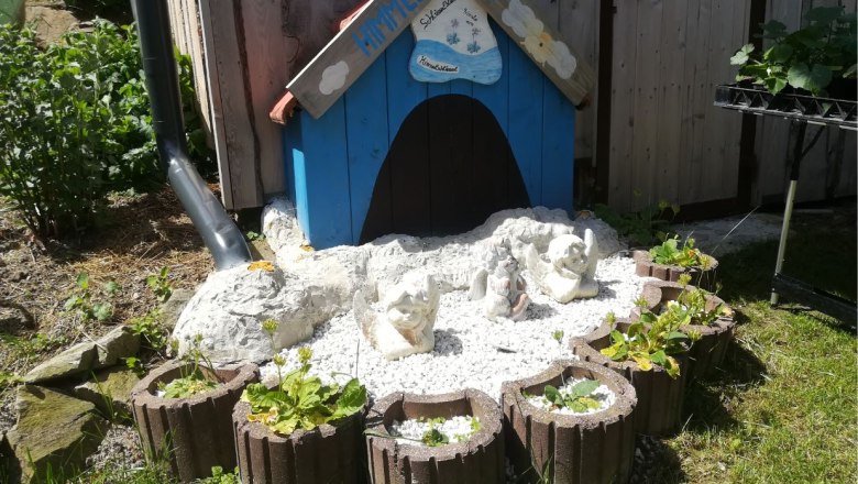 Kleines blaues H&auml;uschen mit Engelfiguren und Pflanzen in einem Garten.