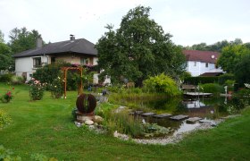 Ein Garten mit Schwimmbiotop, umgeben von Pflanzen und einem Haus im Hintergrund.