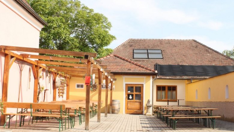 Innenhof einer Weinstube mit Holzb&auml;nken und Tischen unter einer Pergola.