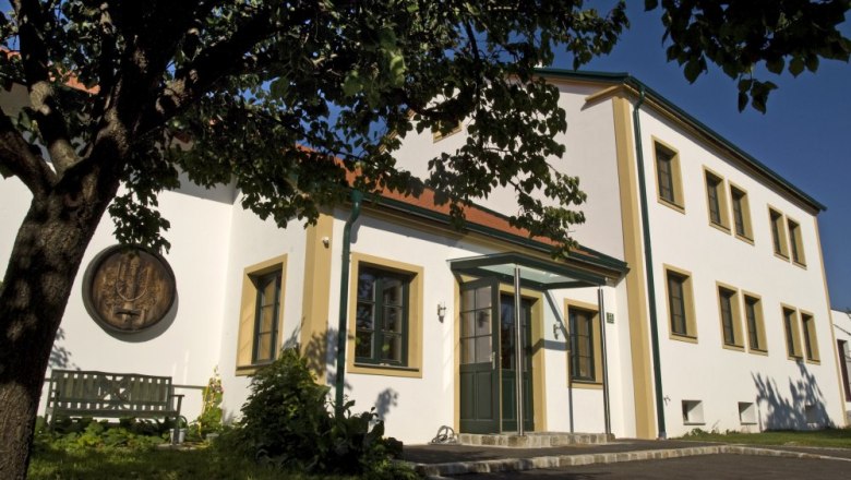 Weingut mit weißer Fassade und grünen Fensterrahmen, umgeben von Bäumen.