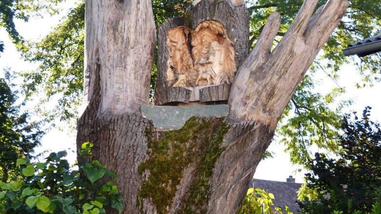 Holzskulptur in Form einer Hand mit geschnitzten Figuren und einem kleinen Turm mit Kreuz.