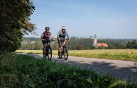 Radfahrer genie&szlig;en die frische Luft und die malerische Landschaft entlang des Kamptal Radwegs. Umgeben von sanften H&uuml;geln und &uuml;ppigen Wiesen, strahlt die Umgebung eine einladende Ruhe aus, die zum Verweilen einl&auml;dt.