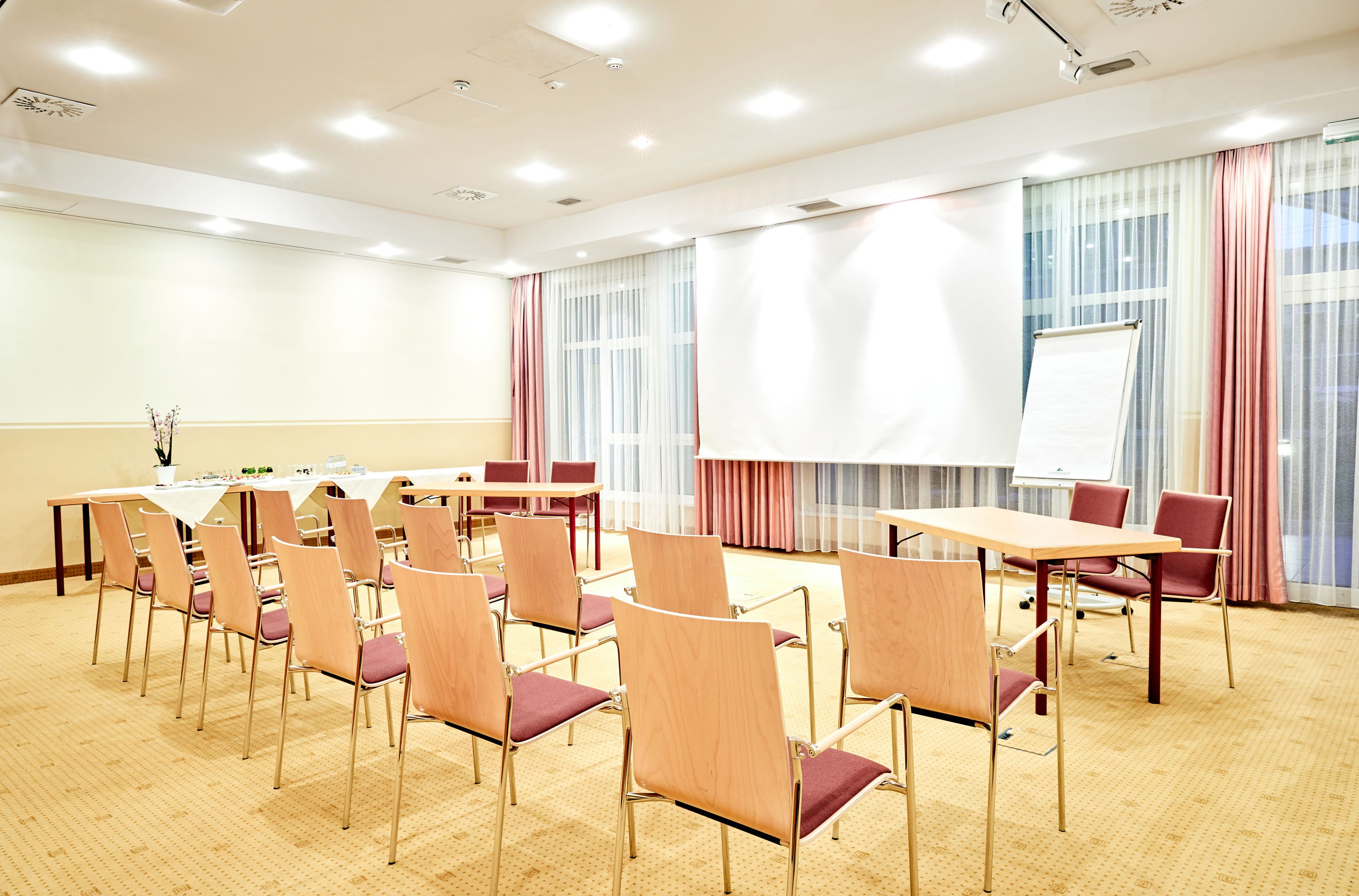 Ein heller Seminarraum mit Stühlen, Tischen, einem Flipchart und einem Projektionsschirm.