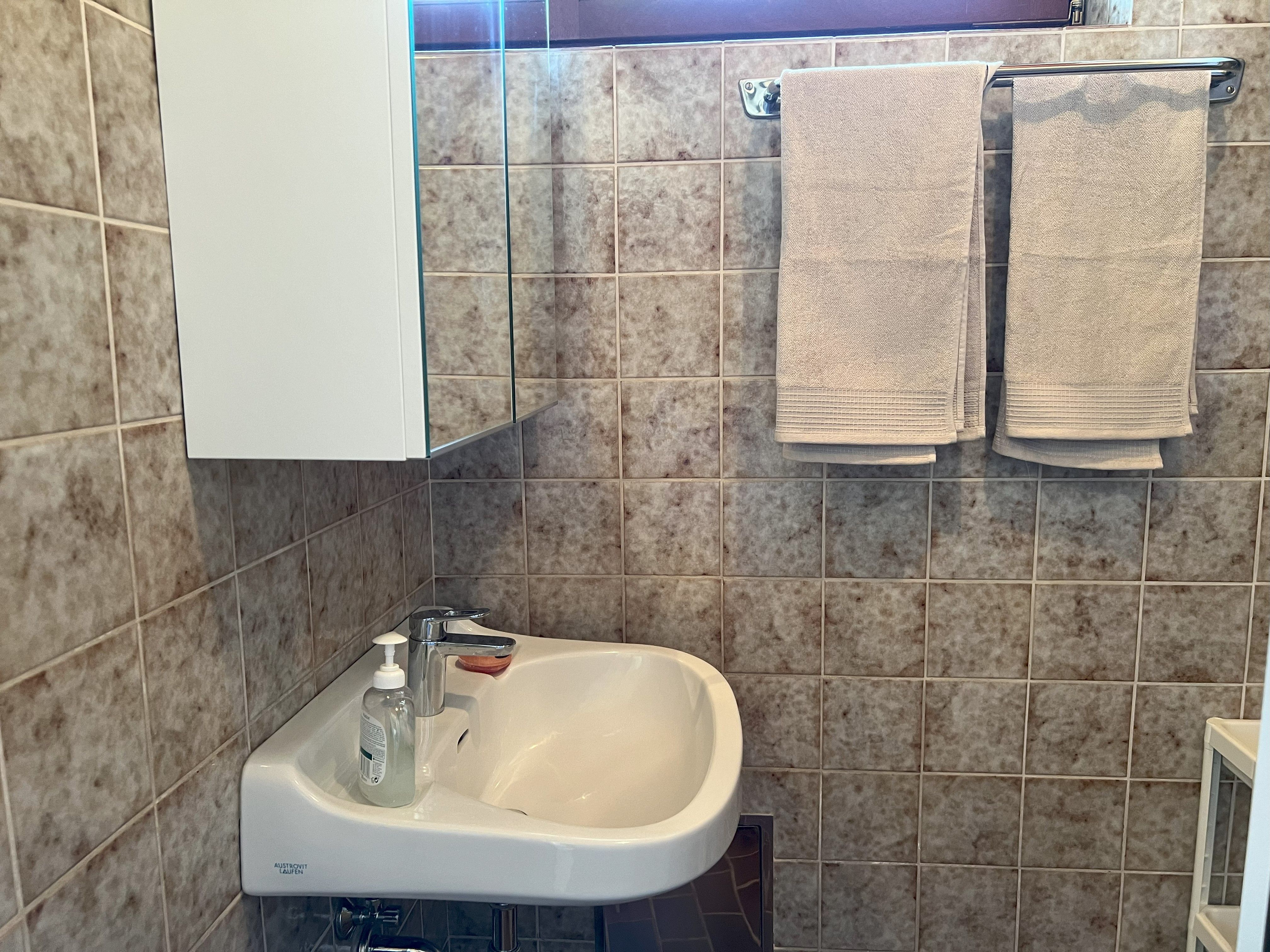 Ein Badezimmer mit Waschbecken, Spiegel, Handtüchern und Fliesen.