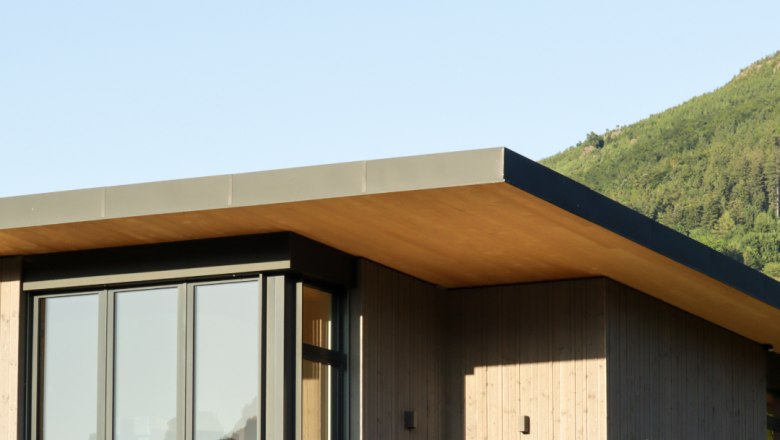 Moderne Lodge mit Flachdach und großen Fenstern, umgeben von grüner Landschaft.