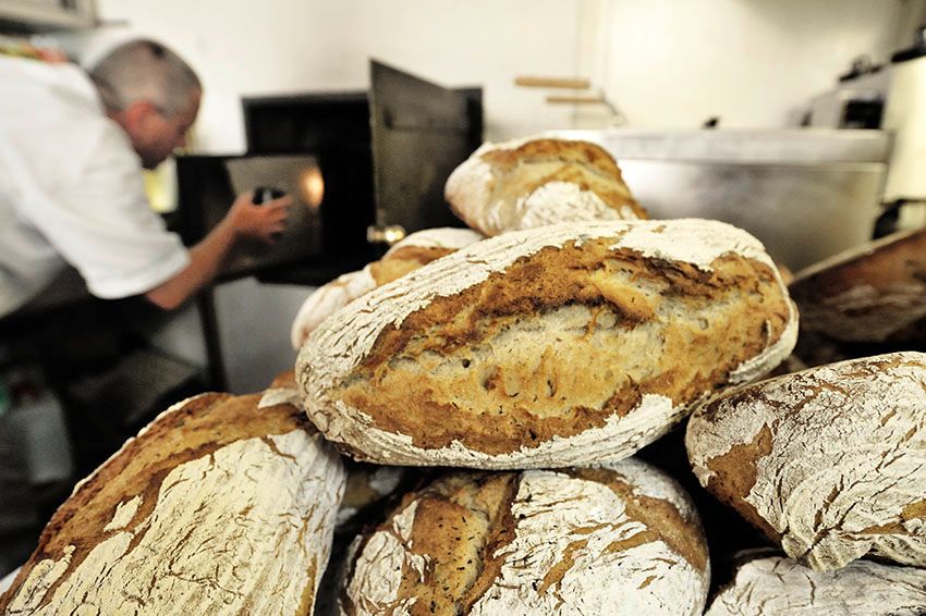 Frisch gebackenes Brot vor einem Bäcker, der einen Ofen bedient.