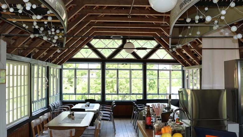 Innenansicht eines hellen Raumes mit Holzdach und großen Fenstern.