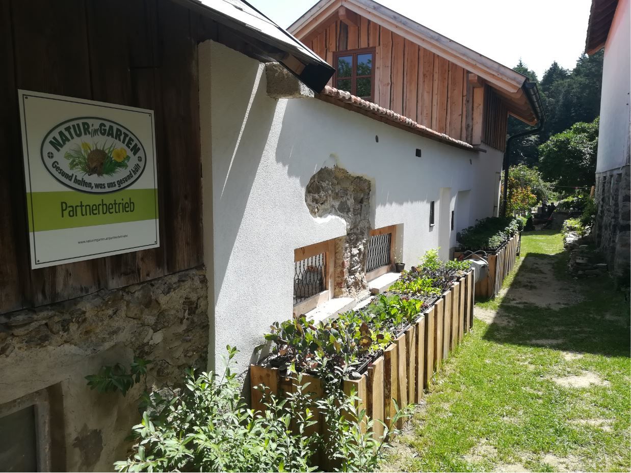 Außenansicht eines Gebäudes mit Schild 'Natur im Garten Partnerbetrieb'.