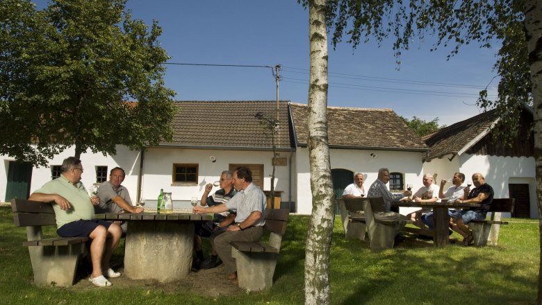 Menschen sitzen an Tischen im Freien vor traditionellen Geb&auml;uden in Sch&ouml;ngrabern.
