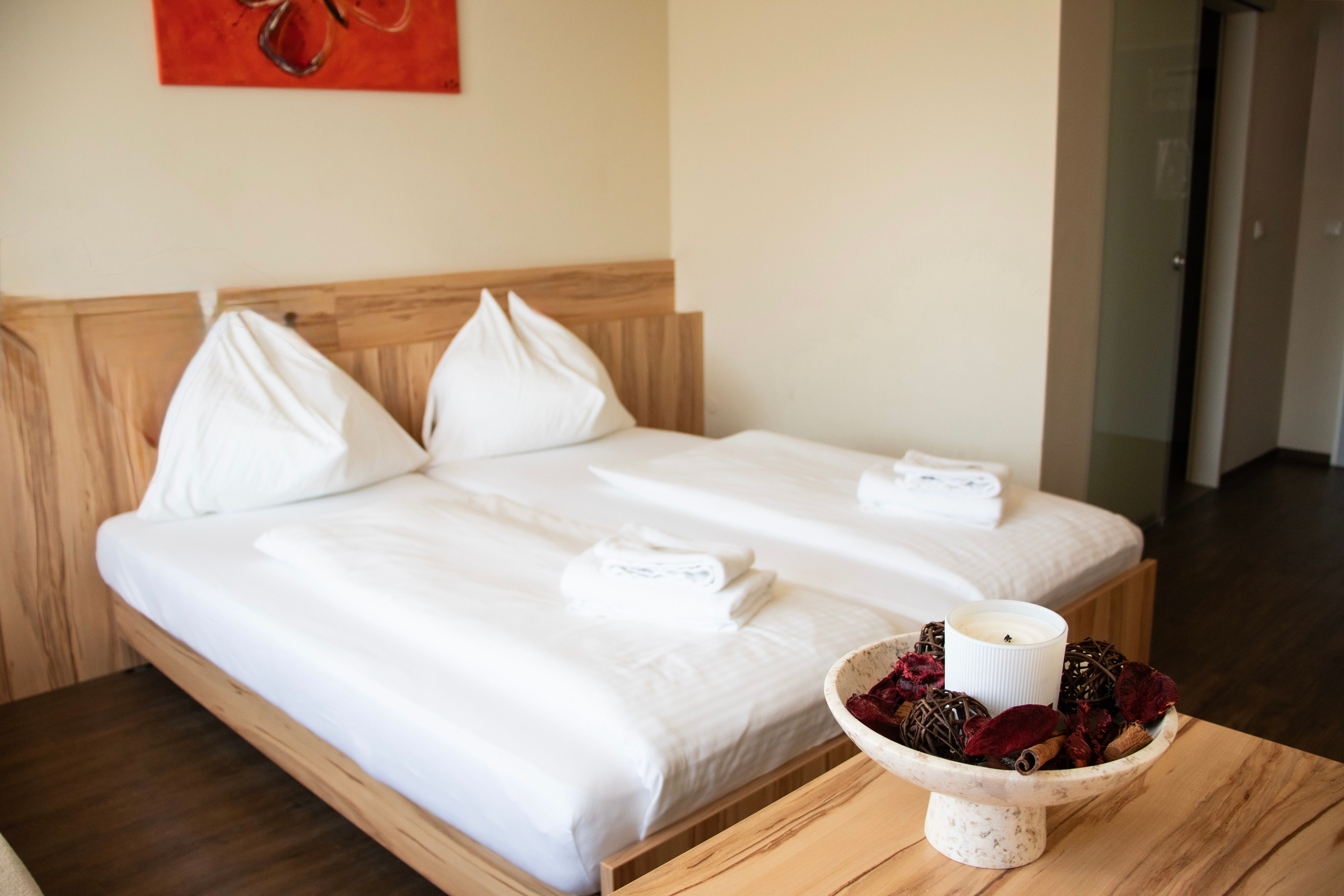 Ein schlichtes Hotelzimmer mit Doppelbett, weißen Handtüchern und dekorativer Schale mit Kerze auf dem Tisch.
