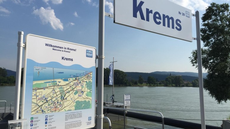 Anlegesteg in Krems mit Willkommensschild und Karte, Fluss im Hintergrund.