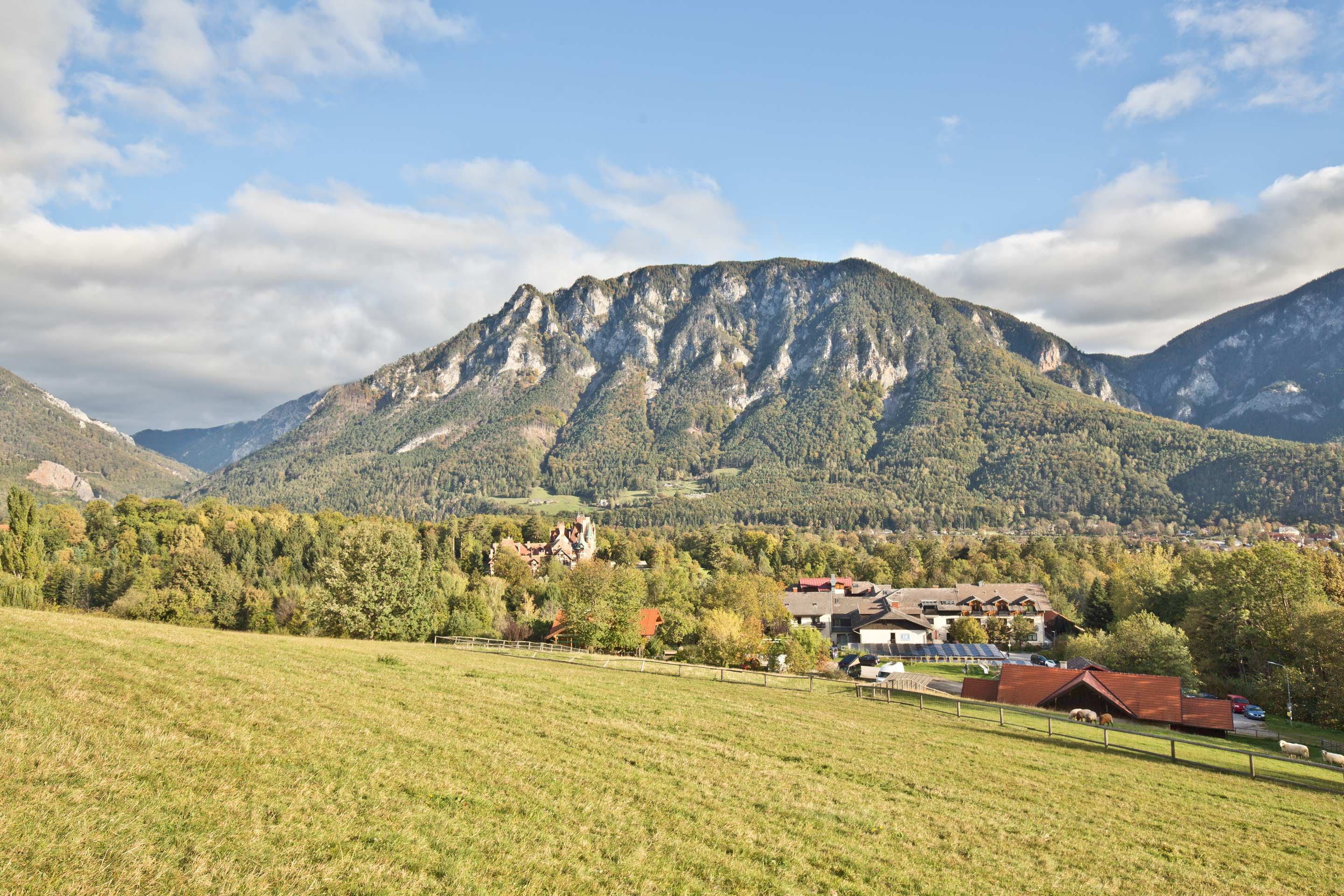 Panoramablick auf eine Berglandschaft mit Wiesen im Vordergrund und einem Dorf im Hintergrund.