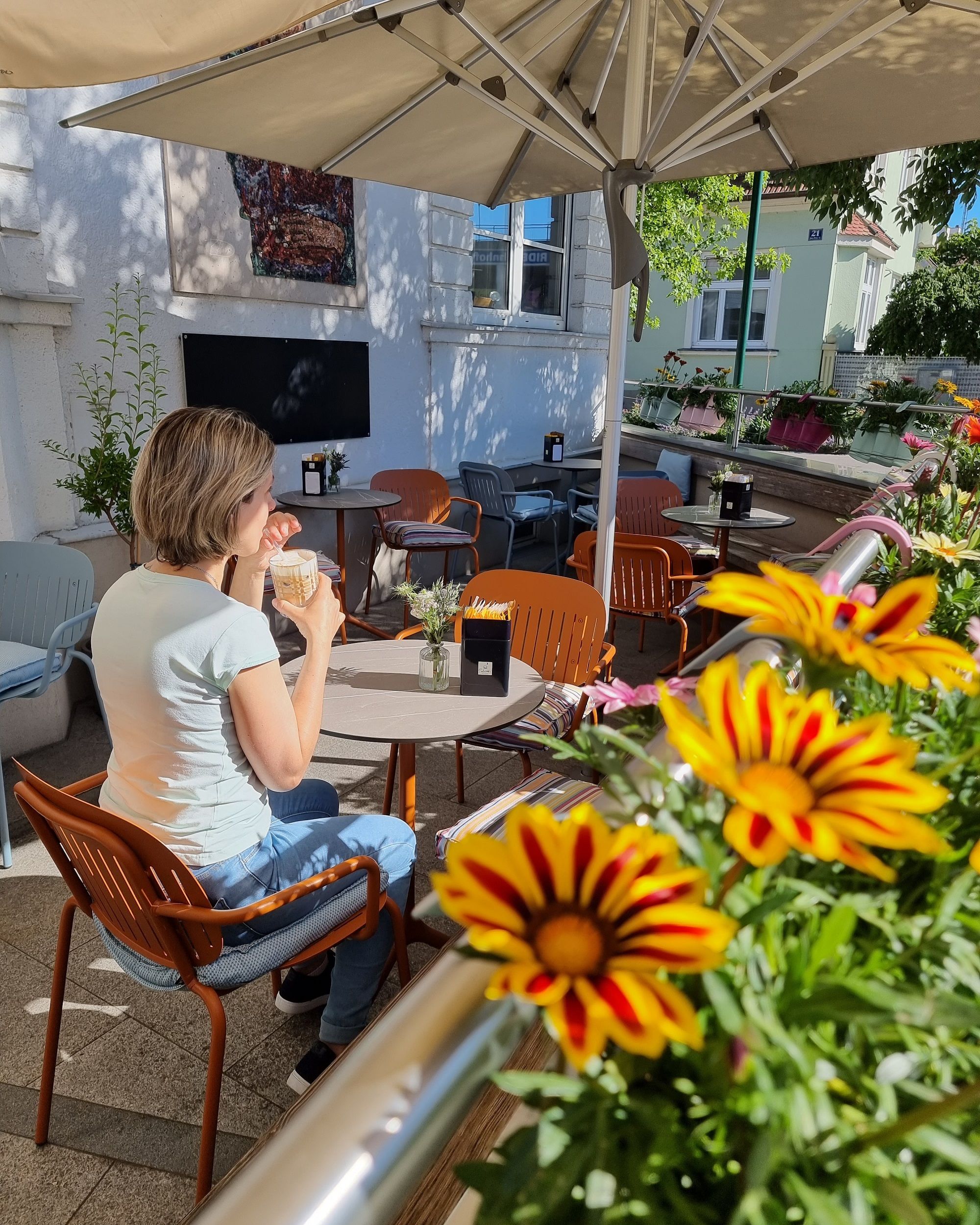 Person von hinten sitzend im Gastgarten mit Kaffee