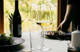 Ein gedeckter Tisch mit Weinflasche, Weingläsern und einem Teller mit Essen in einem Restaurant.