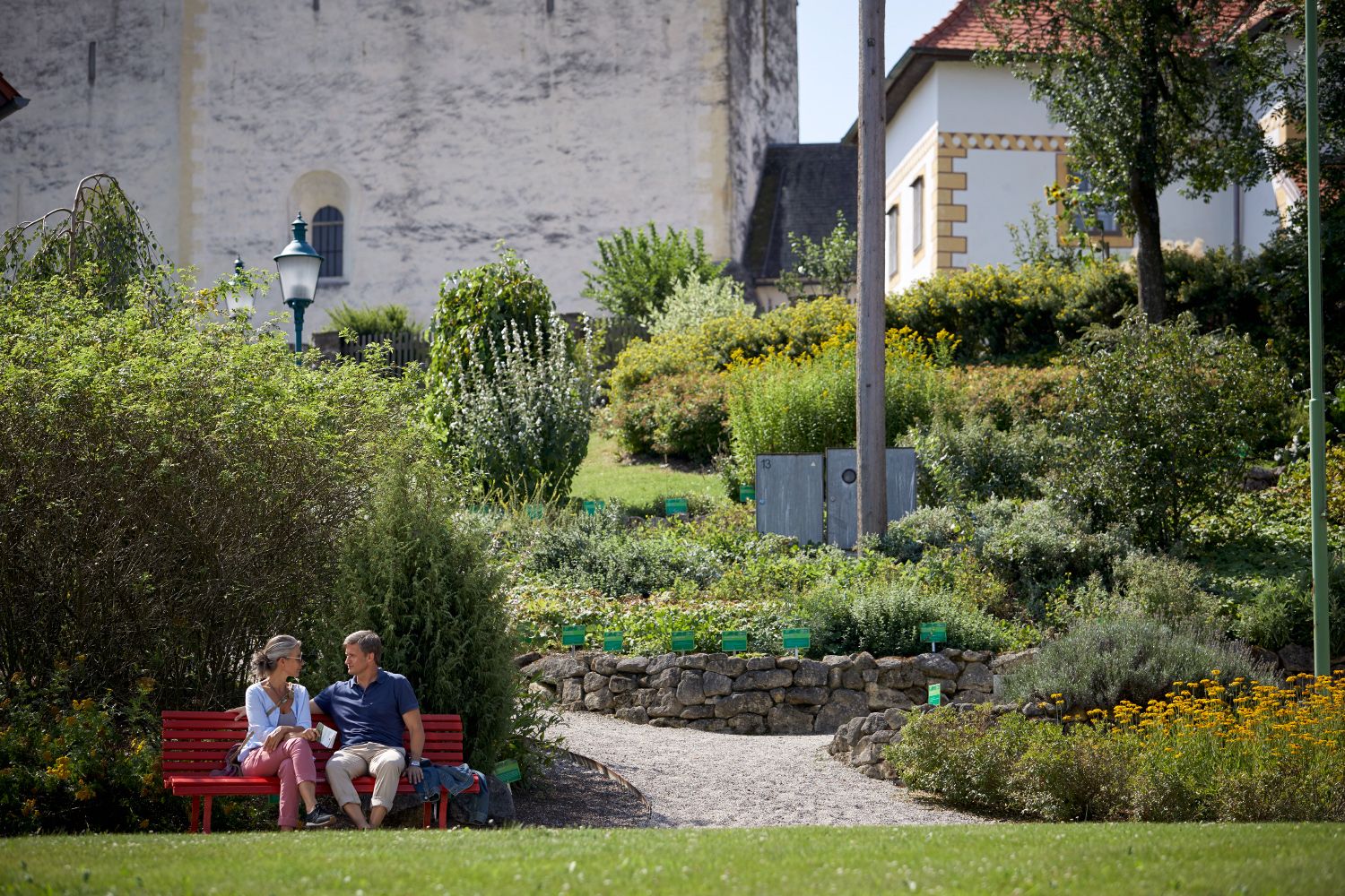 Ein Paar sitzt auf einer roten Bank in einem Garten vor der Wehrkirche Bad Schönau.