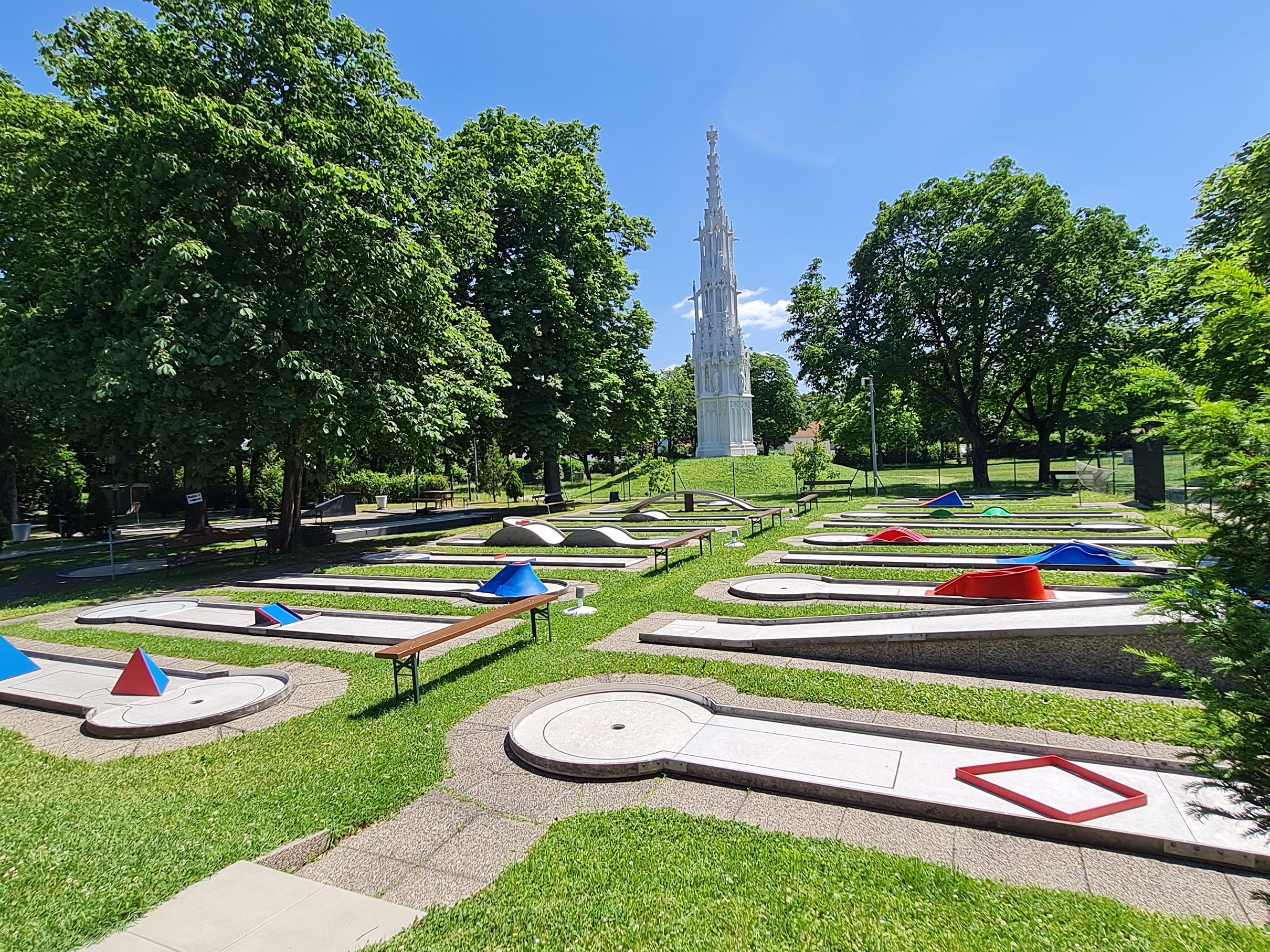 Minigolfplatz mit Hindernissen und einem hohen, weißen Turm im Hintergrund.