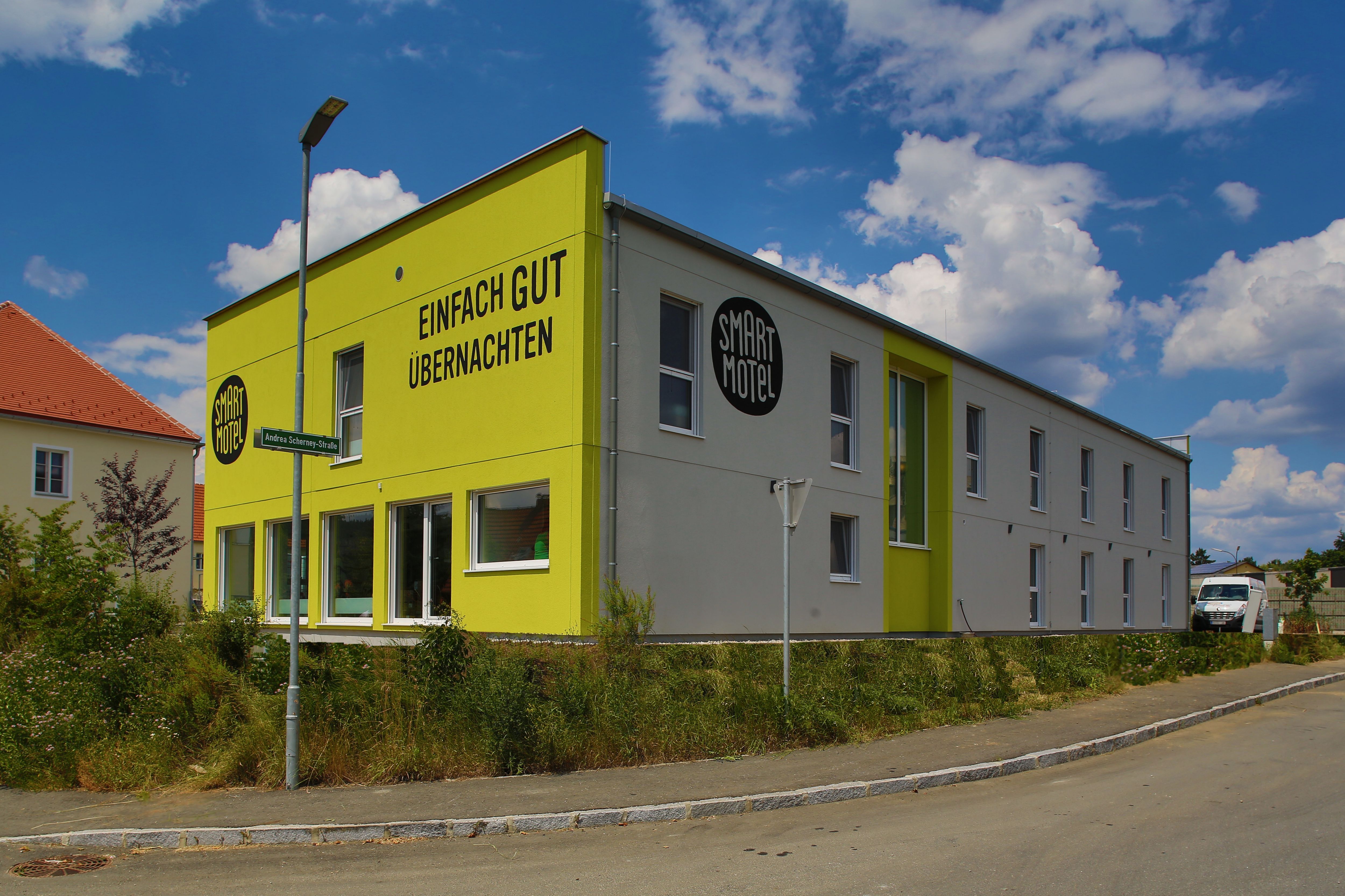 Außenansicht eines modernen, zweistöckigen Motels mit gelber Fassade und der Aufschrift 'Einfach gut übernachten'.