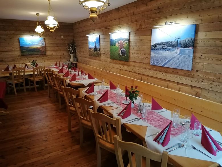 Ein festlich gedeckter Saal mit Holzwänden, dekoriert mit Bildern und roten Servietten auf den Tischen.