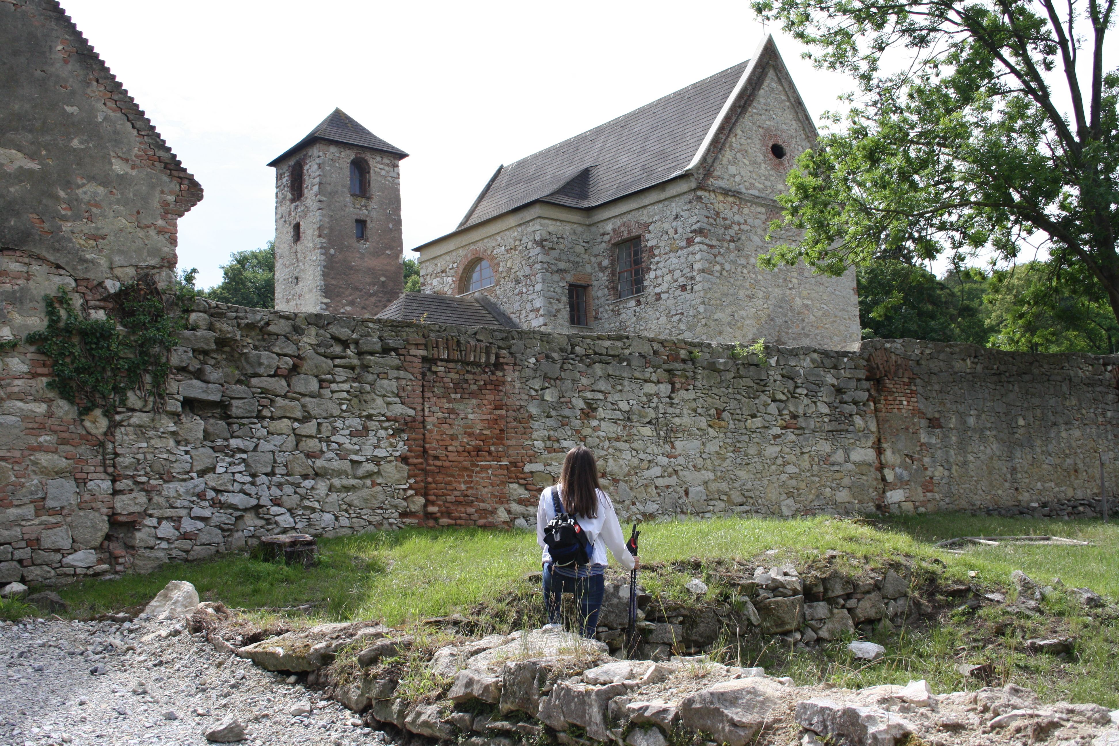 Eine Person steht vor einer alten Steinmauer mit Gebäuden im Hintergrund.