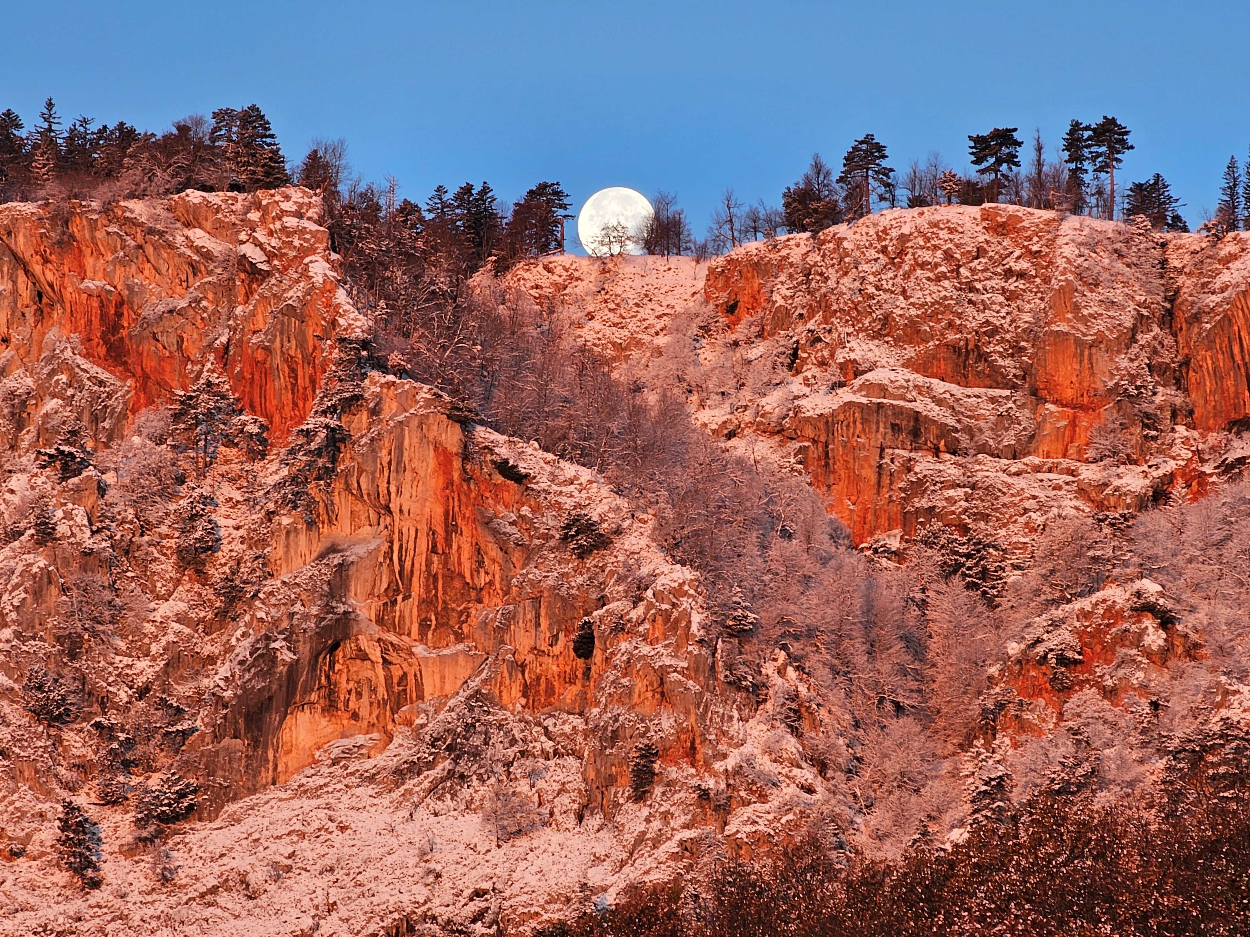 Felswand im Morgenlicht mit Vollmond am Himmel.