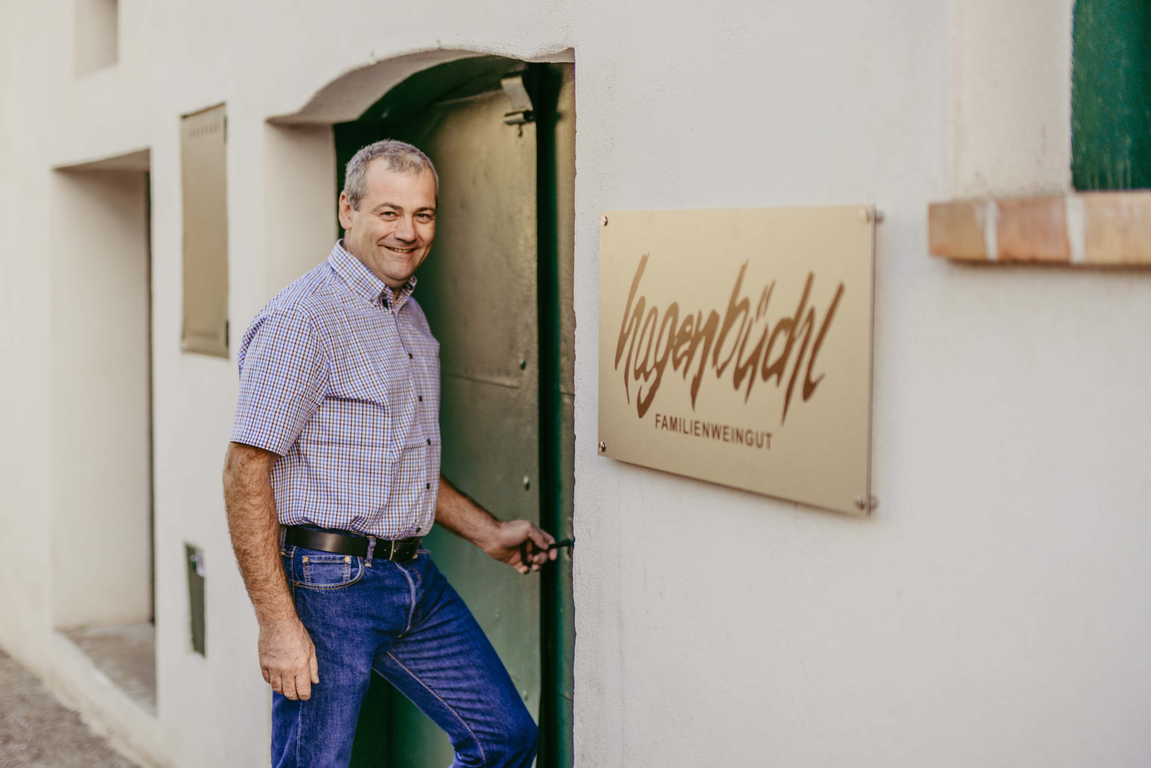 Ein Mann öffnet eine Tür neben einem Schild mit der Aufschrift 'Hagenbüchl Familienweingut'.