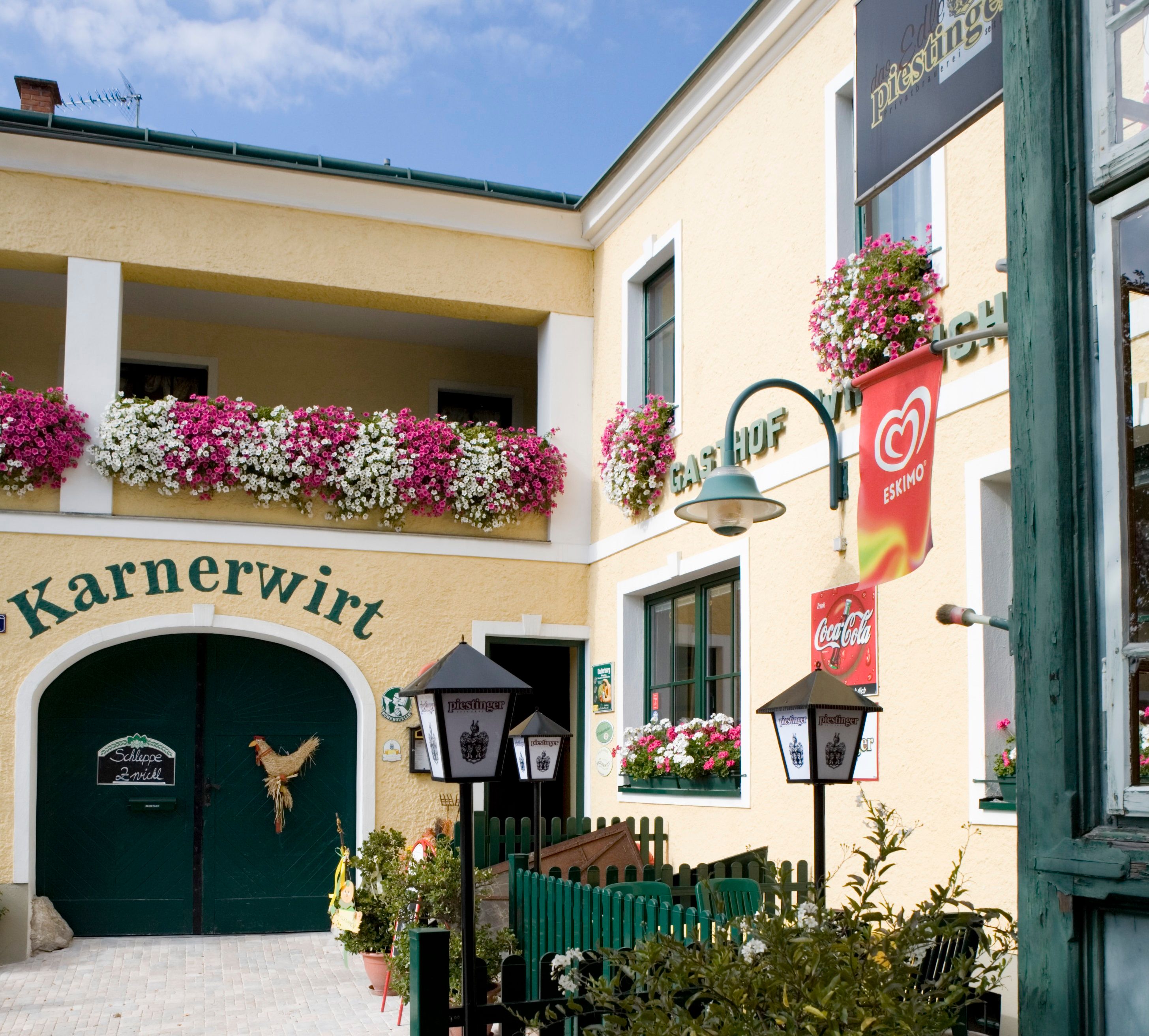 Eingang eines Gasthofs mit Blumen und Werbeschildern.