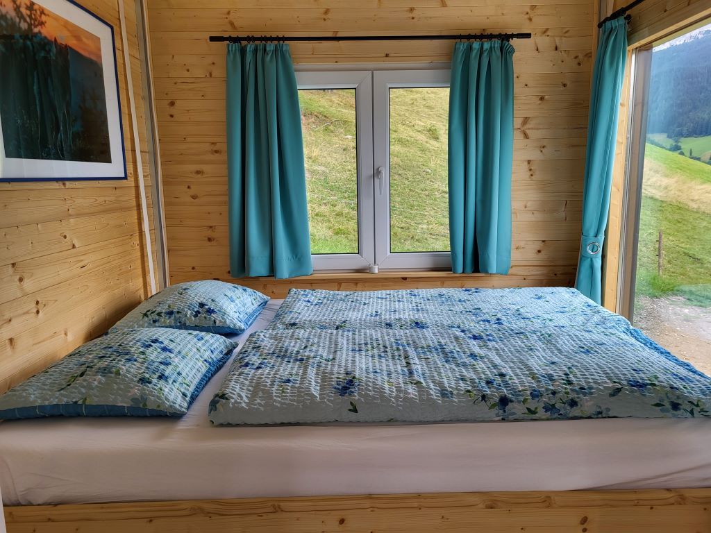 Holzinterieur mit Bett, Fenster und blauen Vorhängen.