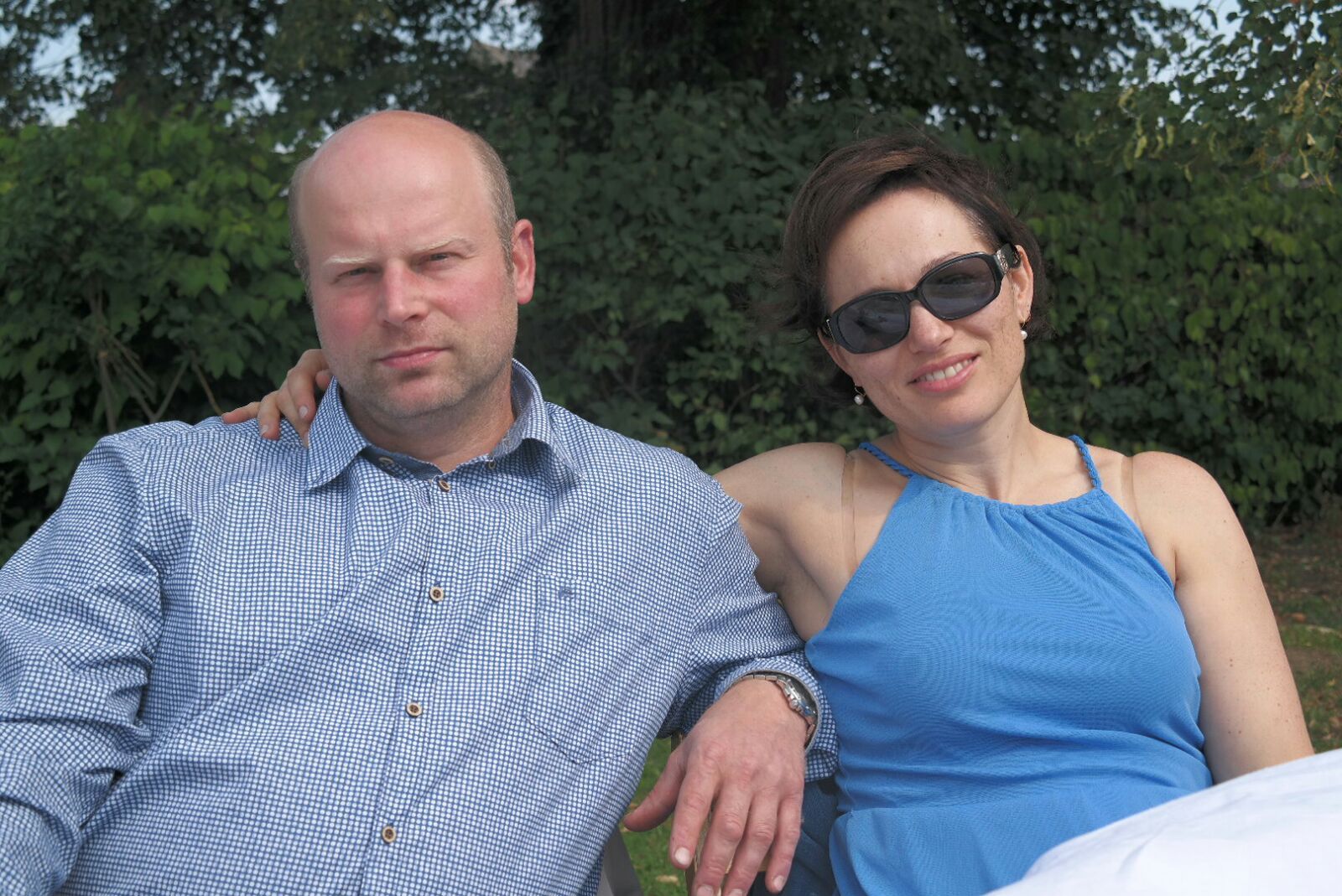 Ein Mann und eine Frau sitzen nebeneinander im Freien, die Frau trägt eine Sonnenbrille.