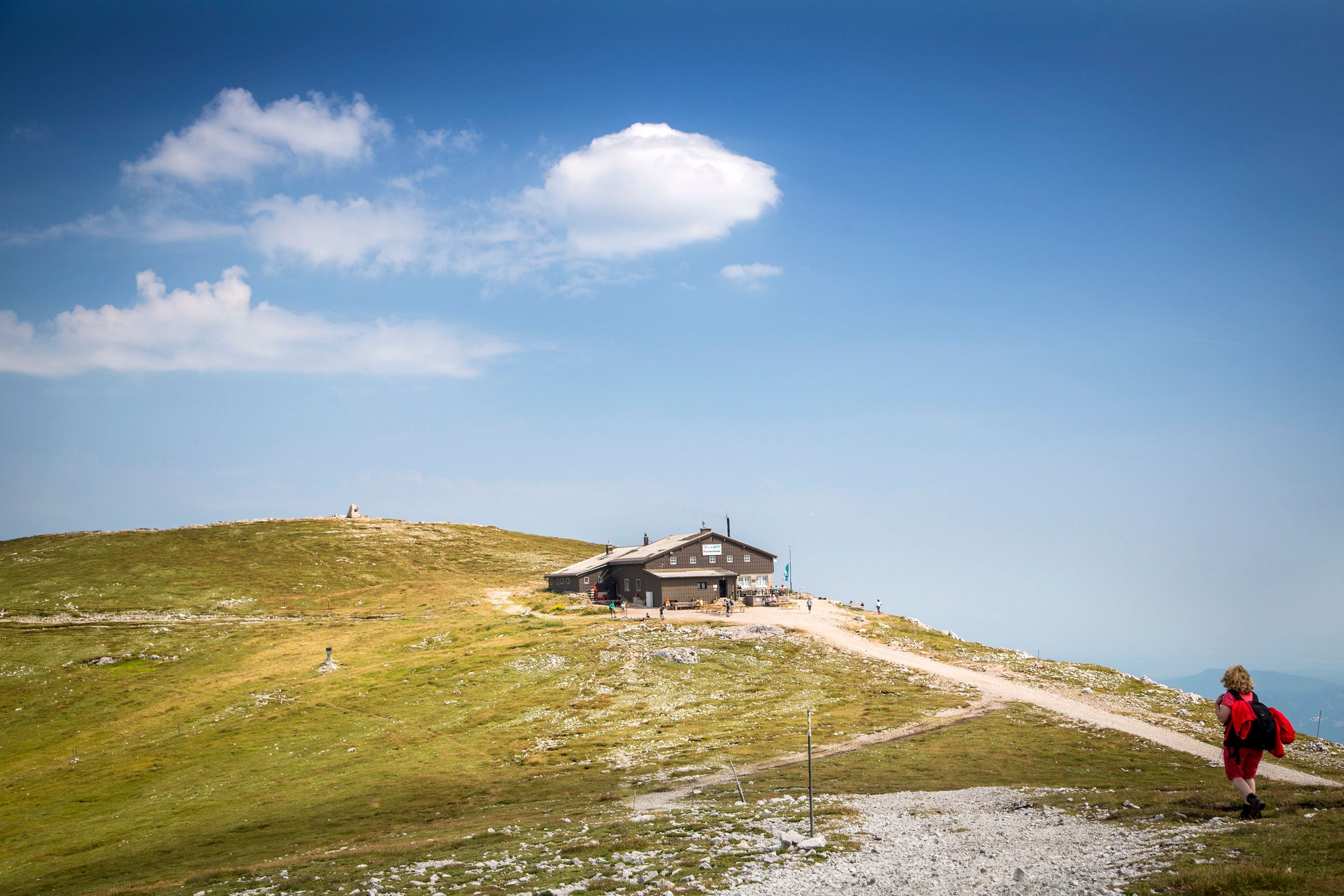 Eine Berghütte auf einem Hügel mit blauem Himmel und Wolken im Hintergrund.