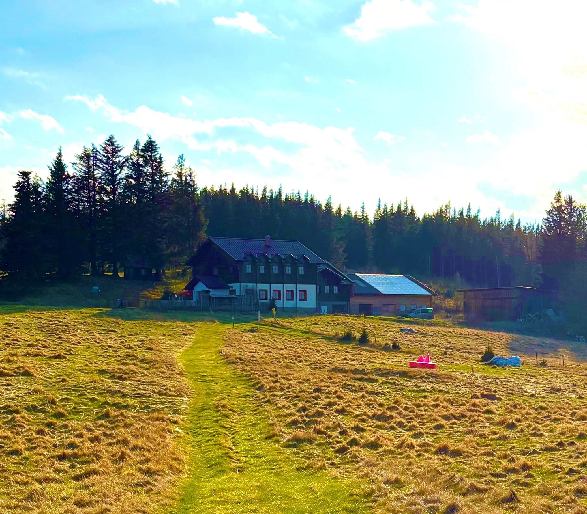 Ein Bauernhaus auf einer Wiese, umgeben von Bäumen und unter einem blauen Himmel.