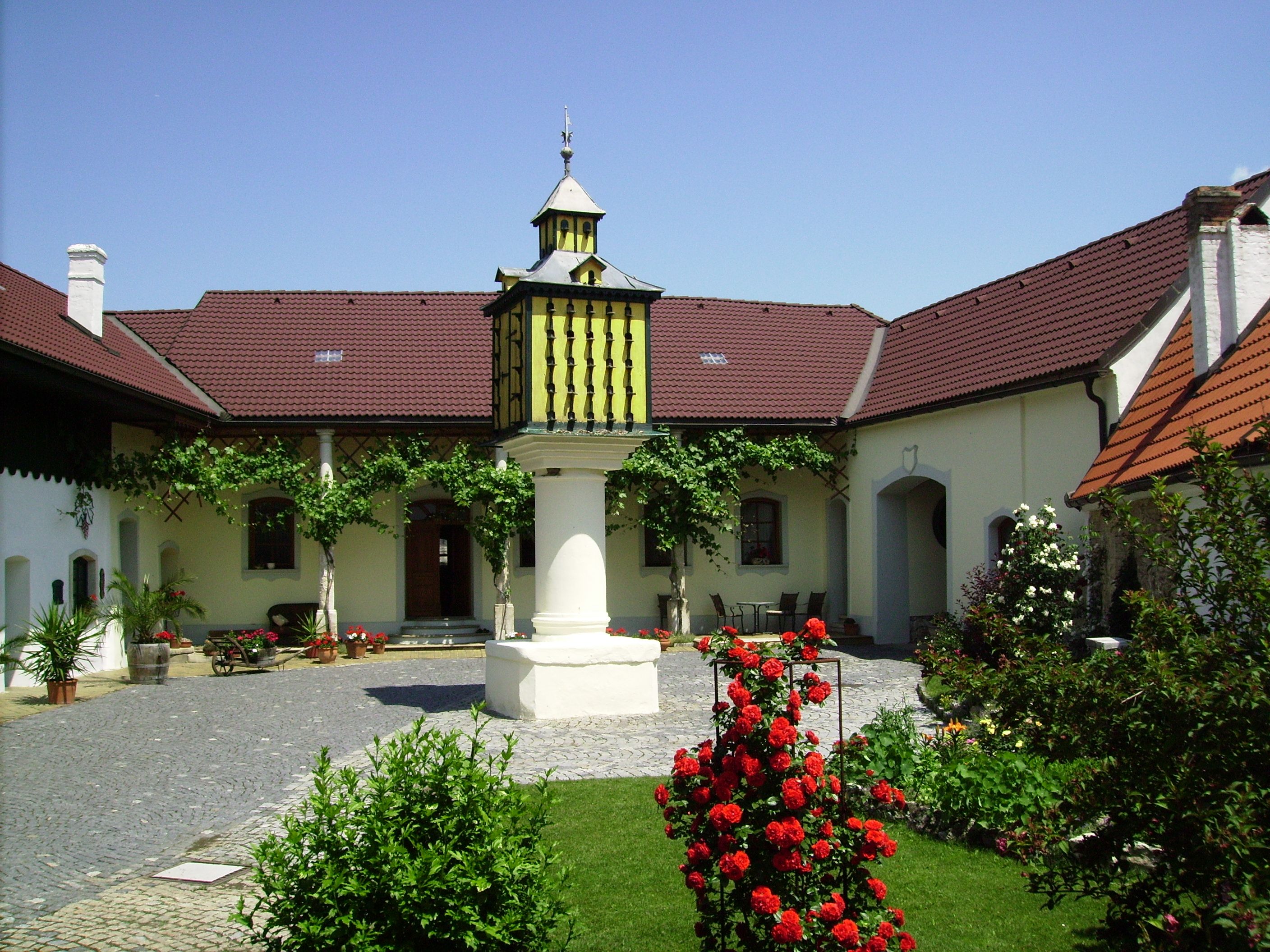 Ein gepflegter Innenhof mit Blumen, einem zentralen Brunnen und einem Gebäude mit roten Dächern.