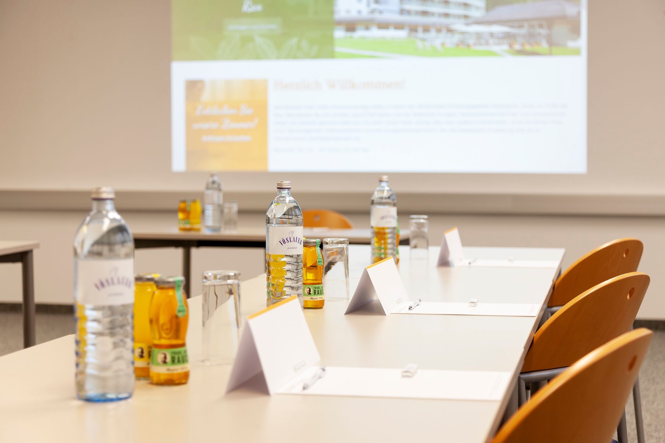 Seminarraum mit Tischen, Stühlen, Wasserflaschen und Notizblöcken.