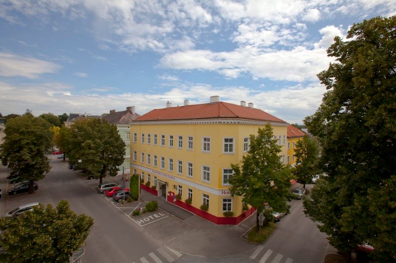 Außenansicht eines gelben Hotels mit rotem Dach, umgeben von Bäumen und Straßen.