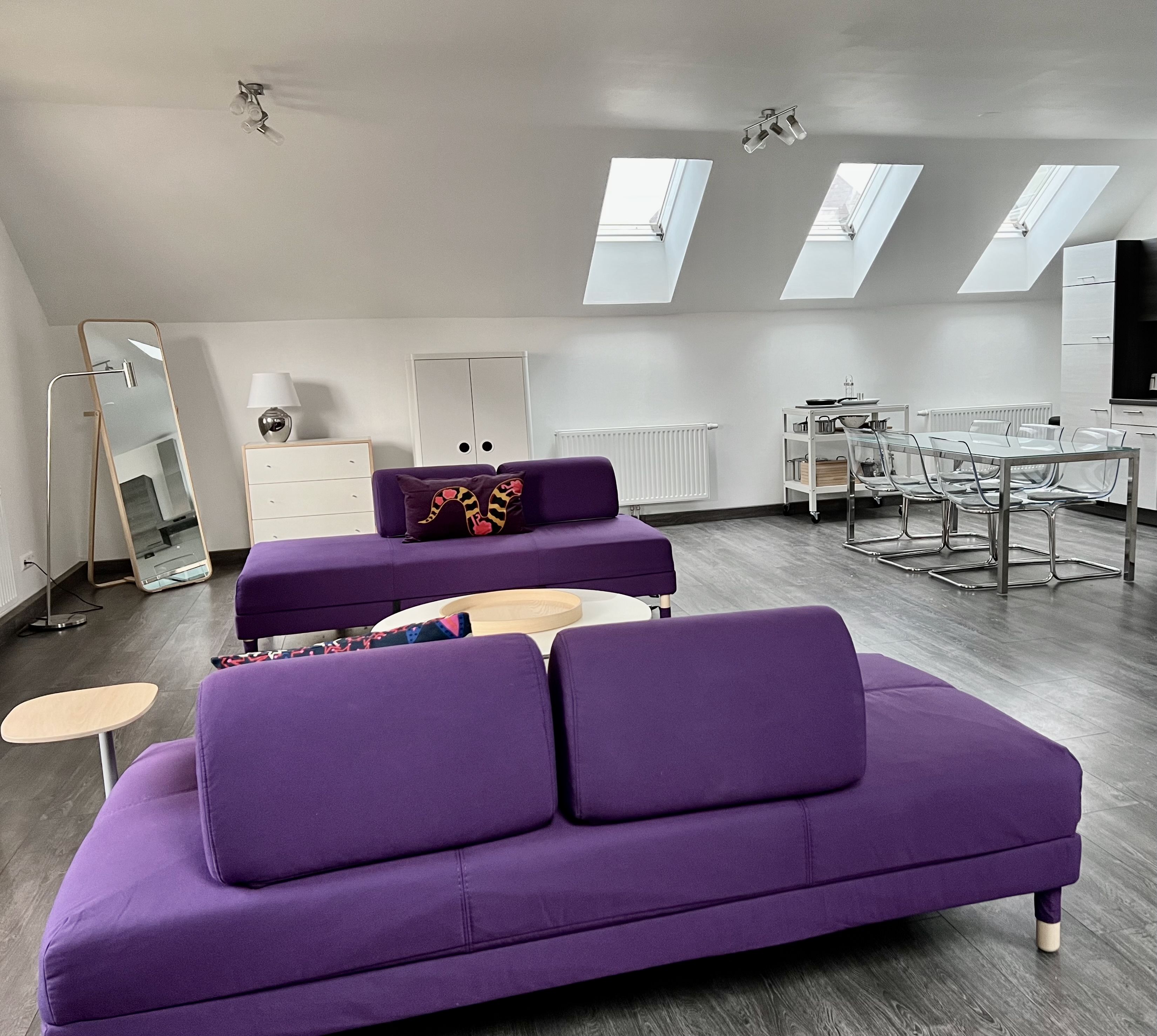 Modernes Loft mit lila Sofas, Esstisch und Dachfenstern.