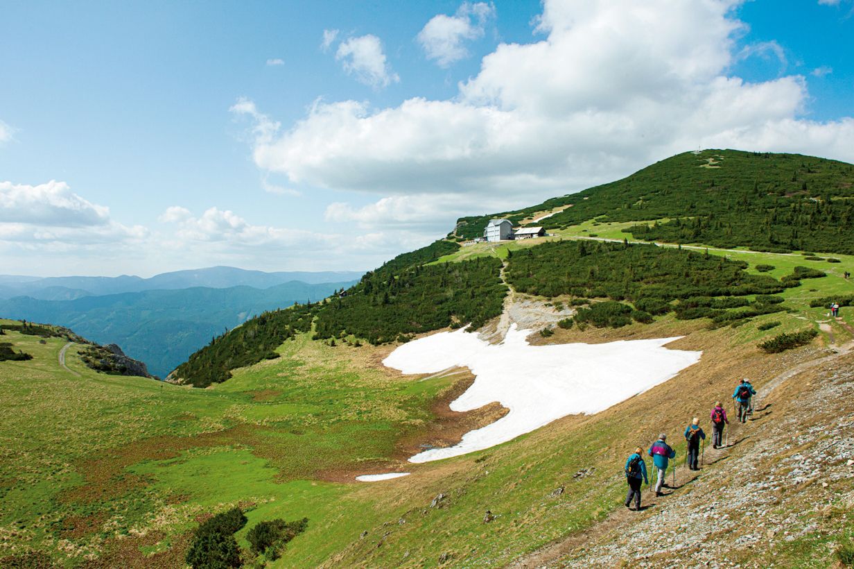 Wanderer auf der Raxalpe mit Schnee und Berghütte im Hintergrund.