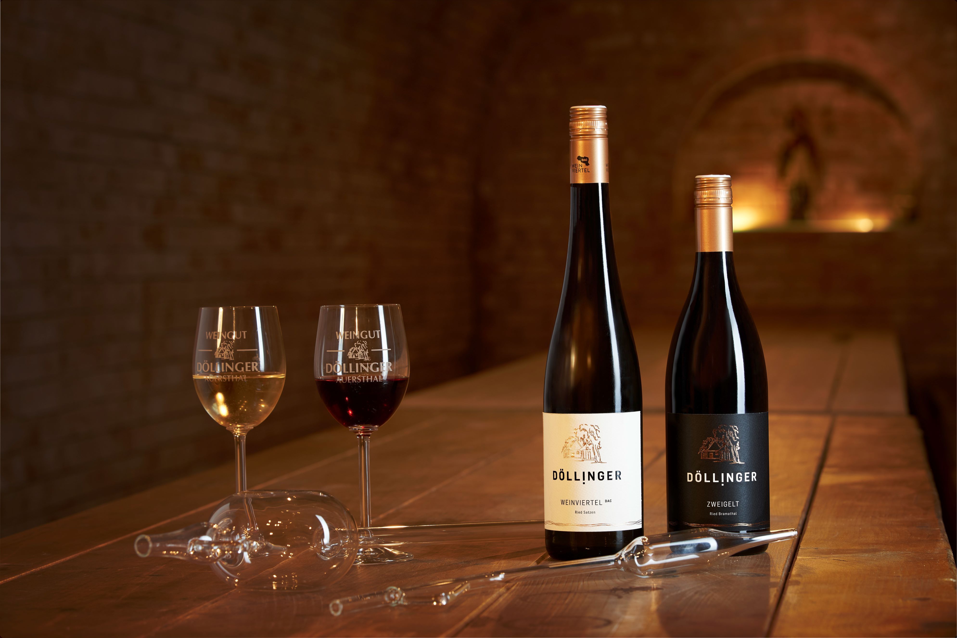 Zwei Weingläser und zwei Flaschen Wein auf einem Holztisch in einem Weinkeller.