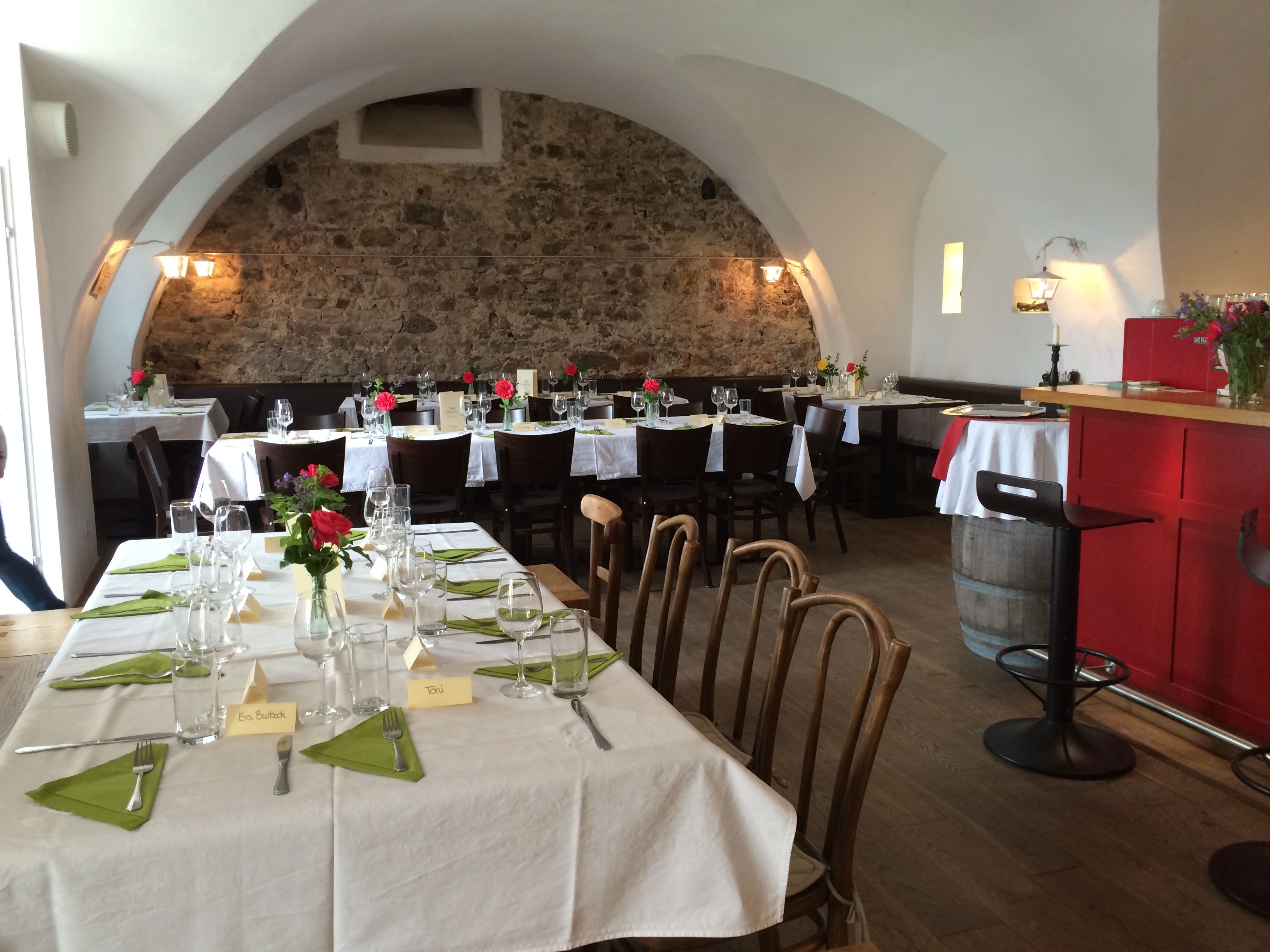 Gemütlicher Gastraum mit gedeckten Tischen, Steinwand und gewölbter Decke.