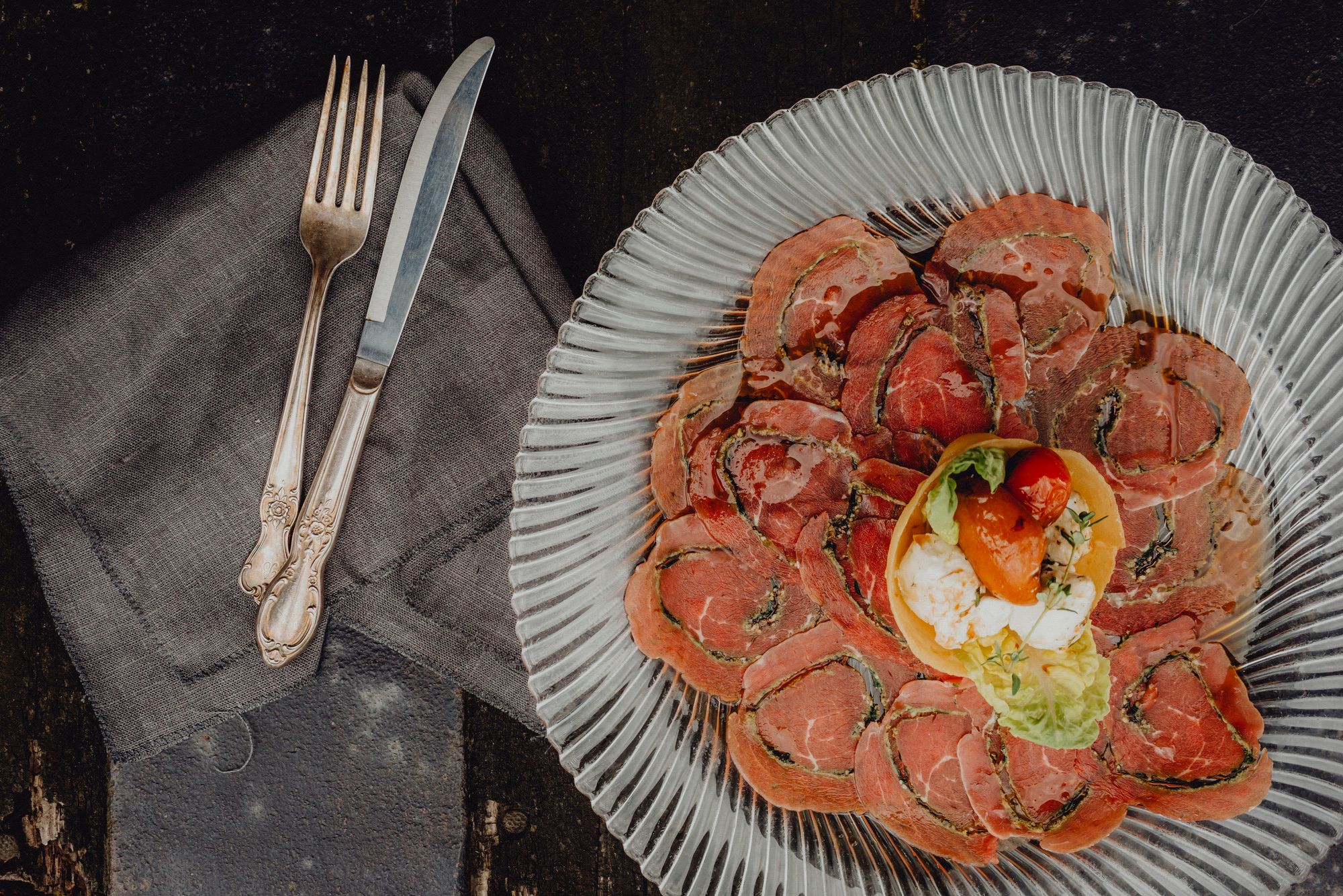 Ein Teller mit dünn geschnittenem Fleisch und einer kleinen Salatgarnitur in der Mitte, daneben Besteck auf einer Serviette.