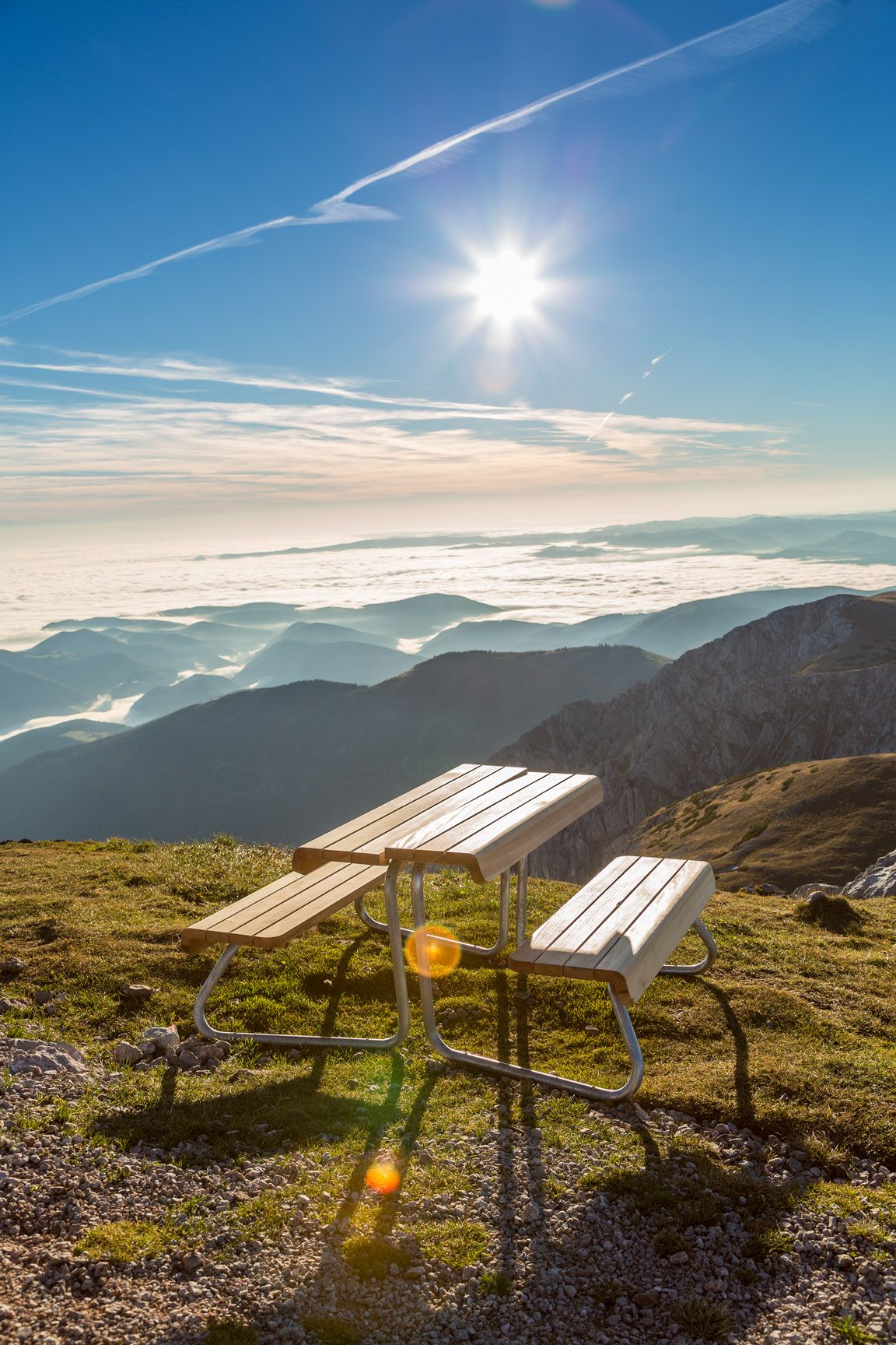 Picknicktisch auf einem Berg mit Blick auf Wolkenmeer und Sonne.