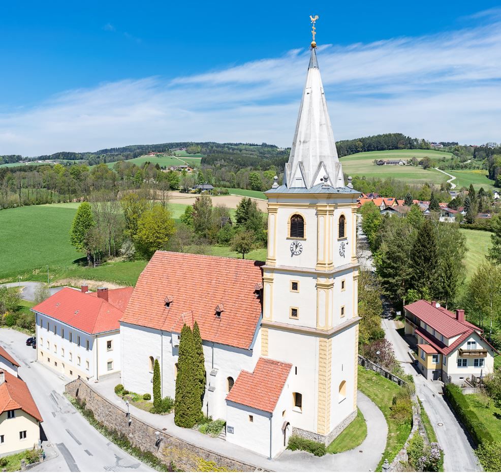 Luftaufnahme der Wehrkirche Krumbach in einer ländlichen Umgebung mit grünen Feldern und blauem Himmel.