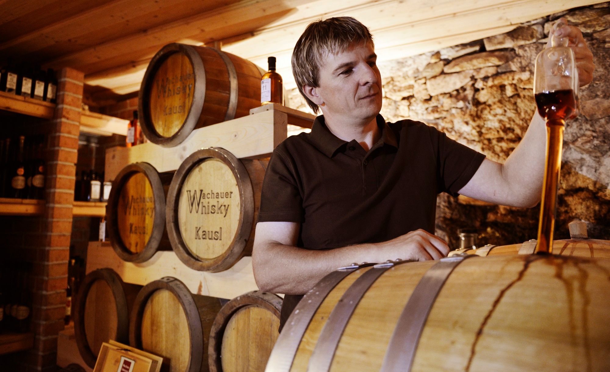 Ein Mann verkostet Whisky in einem Lagerraum mit Fässern.