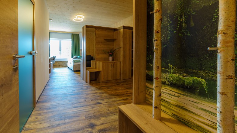 Innenansicht eines modernen Apartments mit Holzboden, Holzm&ouml;beln und einem gro&szlig;en Fenster.