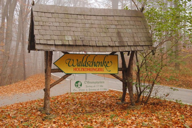 Ein h&ouml;lzernes Schild im Wald weist zur Waldschenke Holzkohlengrill.