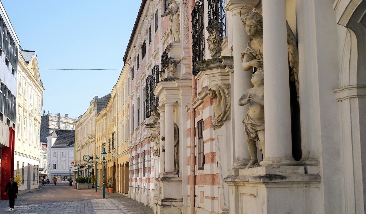 Straße mit historischen Gebäuden und Statuen in einer Stadt.
